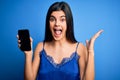 Young beautiful brunette woman wearing blue lingerie holding smartphone showing screen very happy and excited, winner expression Royalty Free Stock Photo