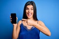 Young beautiful brunette woman wearing blue lingerie holding smartphone showing screen very happy pointing with hand and finger Royalty Free Stock Photo