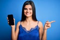 Young beautiful brunette woman wearing blue lingerie holding smartphone showing screen very happy pointing with hand and finger to Royalty Free Stock Photo