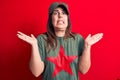 Young beautiful brunette woman wearing cap and t-shirt with red star communist symbol clueless and confused with open arms, no