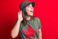 Young beautiful brunette woman wearing cap and t-shirt with red star communist symbol smiling with hand over ear listening and