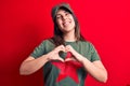 Young beautiful brunette woman wearing cap and t-shirt with red star communist symbol smiling in love doing heart symbol shape