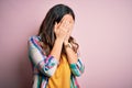 Young beautiful brunette woman wearing casual colorful shirt standing over pink background with sad expression covering face with Royalty Free Stock Photo