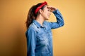 Young beautiful brunette woman wearing casual denim shirt and hair handkerchief very happy and smiling looking far away with hand Royalty Free Stock Photo