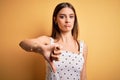 Young beautiful brunette woman wearing casual dress standing over yellow background looking unhappy and angry showing rejection Royalty Free Stock Photo
