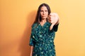 Young beautiful brunette woman wearing casual floral dress standing over yellow background looking unhappy and angry showing Royalty Free Stock Photo