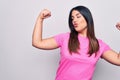 Young beautiful brunette woman wearing casual pink t-shirt standing over white background showing arms muscles smiling proud Royalty Free Stock Photo