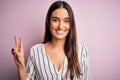 Young beautiful brunette woman wearing casual striped shirt over isolated pink background smiling with happy face winking at the Royalty Free Stock Photo