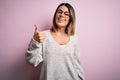 Young beautiful brunette woman wearing casual sweater and glasses over pink background doing happy thumbs up gesture with hand Royalty Free Stock Photo