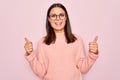 Young beautiful brunette woman wearing casual sweater and glasses over pink background success sign doing positive gesture with Royalty Free Stock Photo