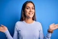 Young beautiful brunette woman wearing casual sweater standing over blue background smiling showing both hands open palms, Royalty Free Stock Photo