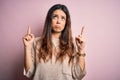 Young beautiful brunette woman wearing casual sweater standing over pink background Pointing up looking sad and upset, indicating Royalty Free Stock Photo