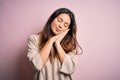 Young beautiful brunette woman wearing casual sweater standing over pink background sleeping tired dreaming and posing with hands Royalty Free Stock Photo