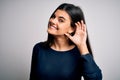 Young beautiful brunette woman wearing casual sweater standing over white background smiling with hand over ear listening an Royalty Free Stock Photo