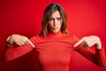 Young beautiful brunette woman wearing casual turtleneck sweater over red background Pointing down looking sad and upset,