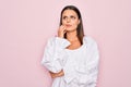 Young beautiful brunette woman wearing casual white dress standing over pink background with hand on chin thinking about question, Royalty Free Stock Photo