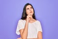 Young beautiful brunette woman wearing casual white t-shirt over purple background with hand on chin thinking about question, Royalty Free Stock Photo