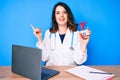 Young beautiful brunette woman wearing doctor uniform holding heart smiling happy pointing with hand and finger to the side Royalty Free Stock Photo