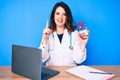 Young beautiful brunette woman wearing doctor uniform holding heart smiling with an idea or question pointing finger with happy Royalty Free Stock Photo