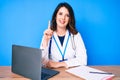 Young beautiful brunette woman wearing doctor uniform working at the clinic smiling with an idea or question pointing finger up Royalty Free Stock Photo