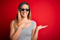 Young beautiful brunette woman wearing funny thug life sunglasses over red background amazed and smiling to the camera while Royalty Free Stock Photo