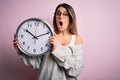 Young beautiful brunette woman wearing glasses doing countdown using big clock scared in shock with a surprise face, afraid and Royalty Free Stock Photo