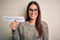 Young beautiful brunette woman wearing glasses holding paper with love yourself message with a happy face standing and smiling Royalty Free Stock Photo