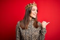 Young beautiful brunette woman wearing golden crown queen over isolated red background smiling with happy face looking and Royalty Free Stock Photo