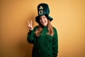 Young beautiful brunette woman wearing green hat on st patricks day celebration smiling with happy face winking at the camera