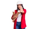 Young beautiful brunette woman wearing hardhat holding architect blueprint with open hand doing stop sign with serious and Royalty Free Stock Photo