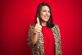 Young beautiful brunette woman wearing a leopard jacket over red isolated background doing happy thumbs up gesture with hand Royalty Free Stock Photo