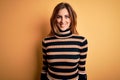 Young beautiful brunette woman wearing striped turtleneck sweater over yellow background with a happy and cool smile on face Royalty Free Stock Photo