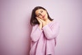 Young beautiful brunette woman wearing a sweater over pink isolated background sleeping tired dreaming and posing with hands Royalty Free Stock Photo