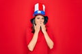 Young beautiful brunette woman wearing united states hat celebrating independence day laughing and embarrassed giggle covering