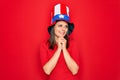 Young beautiful brunette woman wearing united states hat celebrating independence day laughing nervous and excited with hands on