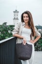 Young beautiful brunette woman wearing in white clothes, holding knitted bag posing in street of city. Copy, empty space for text