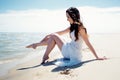 Young beautiful brunette woman in white dress on the seashore. Sitting on the sand Royalty Free Stock Photo