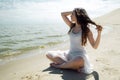 Young beautiful brunette woman in white dress on the seashore, sitting on the sand and looks at horizon Royalty Free Stock Photo