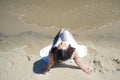 Young beautiful brunette woman in white dress on the seashore, sitting on the sand. Top view Royalty Free Stock Photo