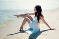 Young beautiful brunette woman in white dress on the seashore. Stroking a leg with a hand Royalty Free Stock Photo