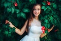 Young beautiful brunette woman in white dress stands on wall background with green leaves and flowers. Royalty Free Stock Photo