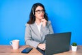 Young beautiful brunette woman working at the office wearing operator headset serious face thinking about question with hand on Royalty Free Stock Photo