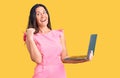 Young beautiful brunette woman working using laptop pointing thumb up to the side smiling happy with open mouth Royalty Free Stock Photo