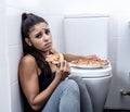 Young beautiful bulimic woman sitting on the bathroom floor eating pizza looking guilty Royalty Free Stock Photo