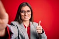 Young beautiful business woman with blue eyes wearing glasses making selfie by camera happy with big smile doing ok sign, thumb up Royalty Free Stock Photo