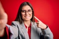 Young beautiful business woman with blue eyes wearing glasses making selfie by camera very happy pointing with hand and finger Royalty Free Stock Photo