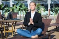 Young beautiful business woman or freelancer takes coffee break at lounge and demonstrates meditation yoga pose Royalty Free Stock Photo