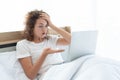 Young beautiful business woman has headache working with laptop while lying in bed in the morning after waking up Royalty Free Stock Photo