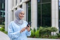 Young beautiful business woman in hijab walks in the city outside the office building, Muslim woman uses an application Royalty Free Stock Photo