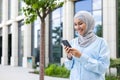 Young beautiful business woman in hijab walks in the city outside the office building, Muslim woman uses an application Royalty Free Stock Photo